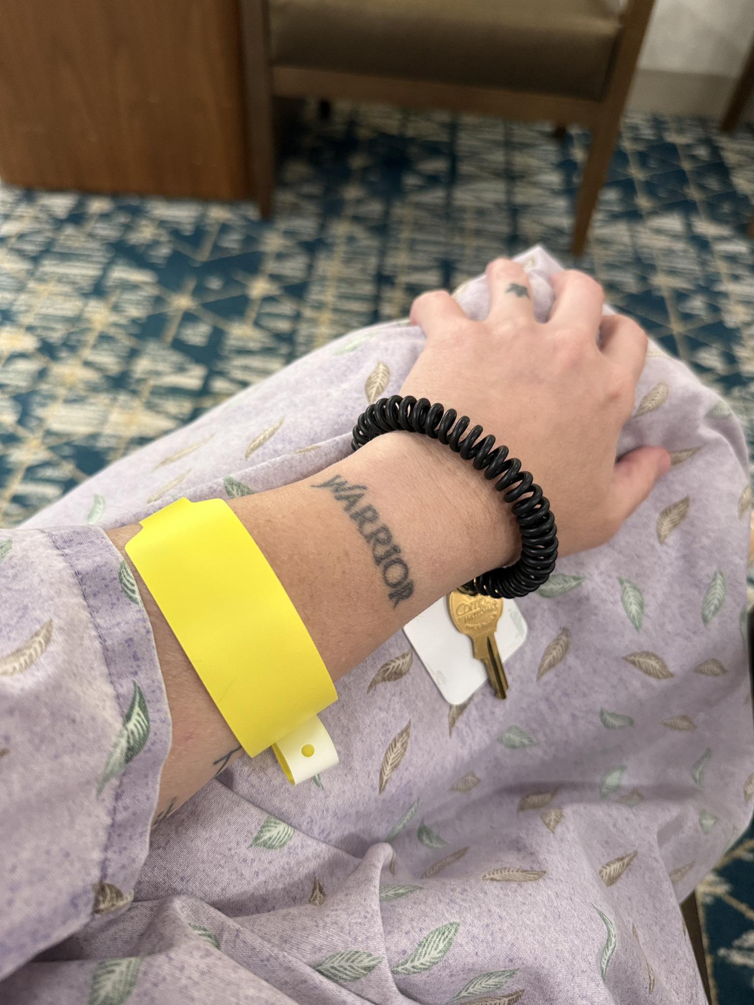 Rachel Minion during treatment, wearing a hospital gown and wristband with a WARRIOR tattoo on her wrist